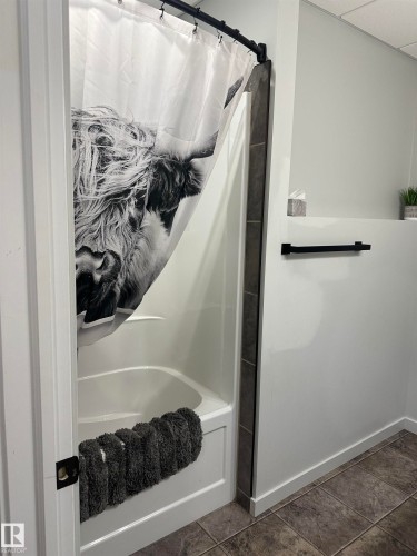 Bathtub with white surround and dark tiled accent, featuring a matte black shower rod and towel bar, set against light gray walls and square floor tiles - 4926 58 Ave, Cold Lake, AB - Indoor Photo Showing Bathroom
