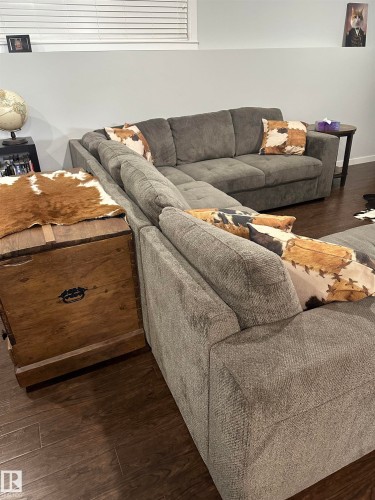 Spacious recreation area featuring wood-finish flooring, light grey walls, and a window with horizontal blinds - 4926 58 Ave, Cold Lake, AB - Indoor Photo Showing Living Room