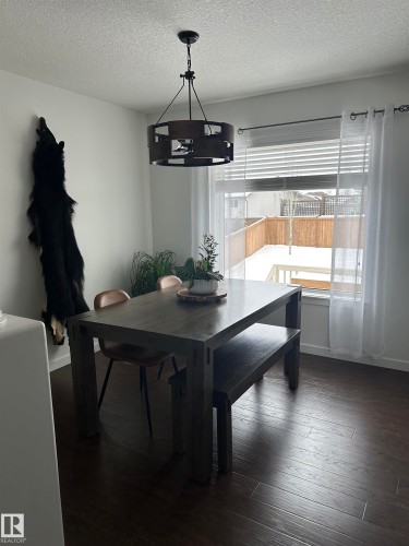 Spacious dining area featuring wood-finish flooring, a contemporary chandelier, a large window with privacy blinds, and light-toned walls - 4926 58 Ave, Cold Lake, AB - Indoor Photo Showing Dining Room