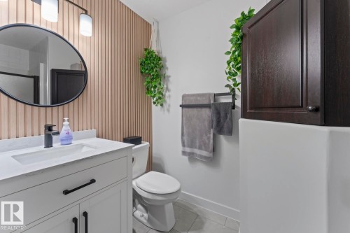 Modern bathroom featuring a white vanity with an integrated sink and matte black hardware, a black-framed circular mirror, and a linear light fixture - 4926 58 Ave, Cold Lake, AB - Indoor Photo Showing Bathroom
