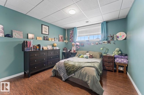 Bedroom featuring wood-finish flooring, a drop ceiling, and a single window with blinds - 4926 58 Ave, Cold Lake, AB - Indoor Photo Showing Bedroom