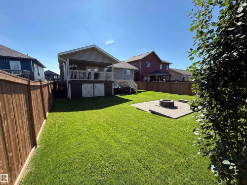 Expansive backyard featuring a manicured lawn, a raised paver patio with a built-in fire pit, and privacy fencing - 4926 58 Ave, Cold Lake, AB - Outdoor With Deck Patio Veranda