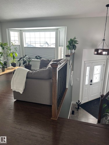 Bay window with cellular shades, wood-finish flooring, staircase with dark wood newel post and balusters, and a decorative pendant light fixture - 4926 58 Ave, Cold Lake, AB - Indoor