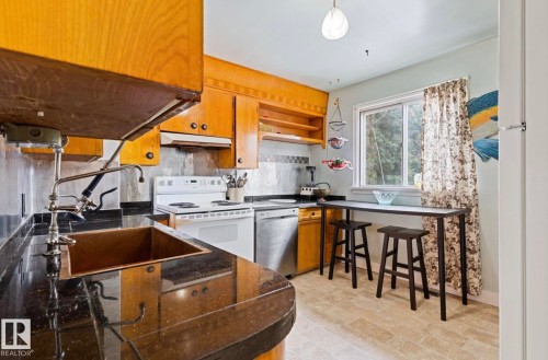 Kitchen featuring wood cabinetry, dark countertops, a copper-toned sink, a tiled backsplash, and light-toned flooring - 7703 77 Avenue, Edmonton, AB 