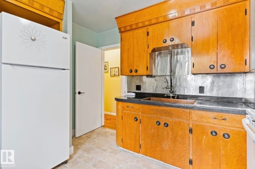 Kitchen featuring light wood cabinetry with round hardware, a stainless steel backsplash, and dark countertops - 7703 77 Avenue, Edmonton, AB 