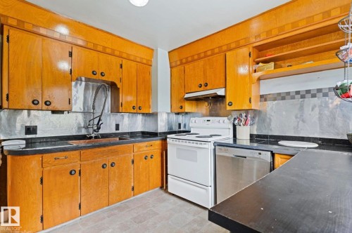 Kitchen featuring wood cabinetry, dark countertops, a stainless steel dishwasher, and an electric range - 7703 77 Avenue, Edmonton, AB 