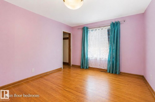 Spacious interior room with wood-finish flooring, a ceiling-mounted light fixture, and a window with a curtain rod - 7703 77 Avenue, Edmonton, AB 