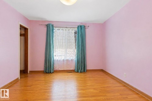 Hardwood flooring highlights this room with a window featuring a white sheer and teal drapes - 7703 77 Avenue, Edmonton, AB 