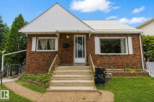 Brick facade residence featuring a white metal roof, concrete front steps with brass-tone railings, and white window shutters - 7703 77 Avenue, Edmonton, AB 