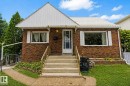 Brick facade residence featuring a white metal roof, concrete front steps with brass-tone railings, and white window shutters - 7703 77 Avenue, Edmonton, AB 
