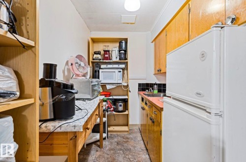 Galley kitchen with wood cabinetry, black subway tile backsplash, and a built-in shelving unit - 7703 77 Avenue, Edmonton, AB 