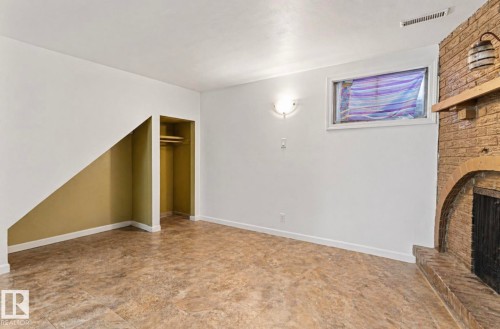 Interior space featuring a brick fireplace with a wood mantle, a window, a wall-mounted sconce, and textured flooring - 7703 77 Avenue, Edmonton, AB 
