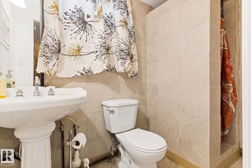 Bathroom featuring a pedestal sink with chrome fixtures, a toilet, and a tiled shower stall - 7703 77 Avenue, Edmonton, AB 