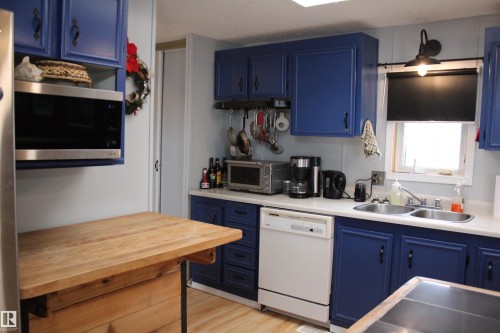 Kitchen featuring blue cabinetry with black hardware, a stainless steel over-the-range microwave, and a double basin sink - 4839 49 Avenue, Chipman, AB - Indoor Photo Showing Kitchen With Double Sink
