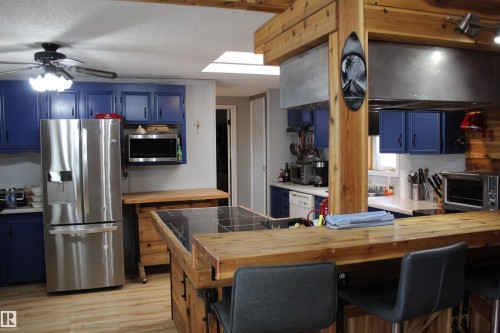 Kitchen featuring exposed wood beams, wood-finish flooring, a skylight, stainless steel refrigerator, and blue cabinetry - 4839 49 Avenue, Chipman, AB - Indoor