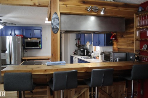 Kitchen featuring a wood-finish breakfast bar, exposed wood beams, blue cabinetry, stainless steel appliances, and a large range hood - 4839 49 Avenue, Chipman, AB - Indoor