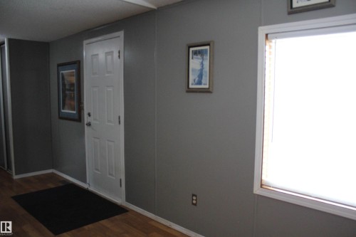 Interior hallway with wood-finish flooring, light gray paneled walls, white trim, and a prominent white paneled door - 4839 49 Avenue, Chipman, AB - Indoor Photo Showing Other Room