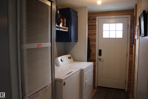 Utility area featuring a side-by-side washer and dryer, a dark blue wall-mounted cabinet, and a wall-mounted heating unit - 4839 49 Avenue, Chipman, AB - Indoor Photo Showing Laundry Room