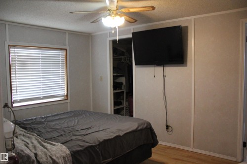 Bedroom featuring wood-finish flooring, a window with blinds, a ceiling fan, and a built-in closet with shelving - 4839 49 Avenue, Chipman, AB - Indoor Photo Showing Bedroom