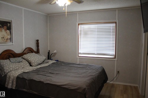 Bedroom featuring a wood-finish bed frame, light gray walls with vertical trim, a large window with white blinds, and light wood-finish flooring - 4839 49 Avenue, Chipman, AB - Indoor Photo Showing Bedroom