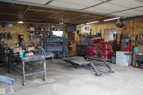Spacious garage with an overhead door, concrete flooring, exposed plywood walls, and overhead lighting - 4839 49 Avenue, Chipman, AB - Indoor Photo Showing Garage