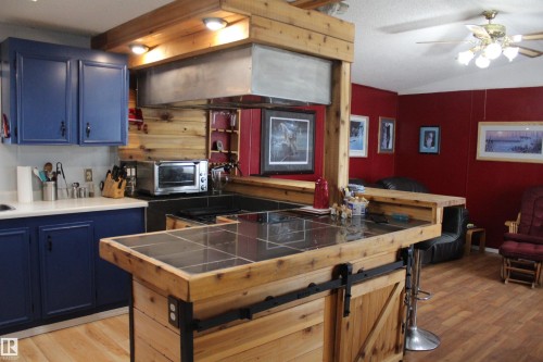 Kitchen featuring blue cabinetry, white countertops, built-in cooktop, wood-finish flooring, and a tile-top island with a barn door accent - 4839 49 Avenue, Chipman, AB - Indoor Photo Showing Kitchen