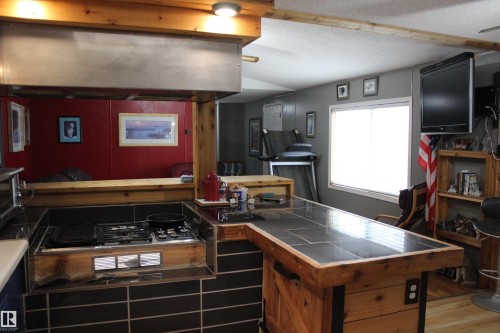 Custom kitchen island featuring a built-in cooktop with an integrated ventilation hood, wood-finish cabinetry, and a tile-top counter - 4839 49 Avenue, Chipman, AB - Indoor