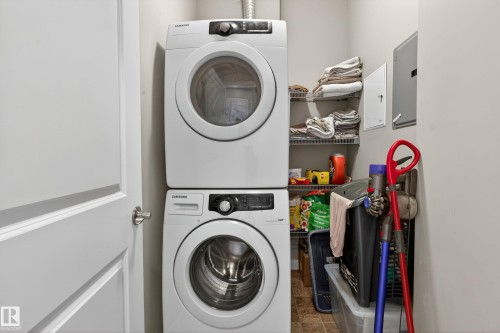 Dedicated laundry area featuring a stacked washer and dryer, adjacent shelving, and light-toned walls - 409 2584 Anderson Way, Edmonton, AB - Indoor Photo Showing Laundry Room