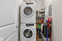 Dedicated laundry area featuring a stacked washer and dryer, adjacent shelving, and light-toned walls - 