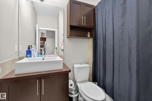 Bathroom featuring a white rectangular vessel sink, dark wood-finish vanity, wall-mounted mirror, and overhead storage cabinetry - 409 2584 Anderson Way, Edmonton, AB - Indoor Photo Showing Bathroom