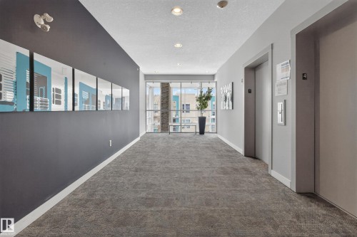 Well-lit corridor featuring recessed lighting, full-height windows, elevator access, and textured gray carpeting - 409 2584 Anderson Way, Edmonton, AB - Indoor Photo Showing Other Room
