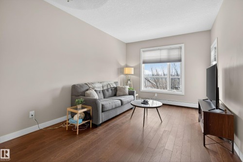 Spacious living area featuring wood-finish flooring, neutral wall tones, and a large window with privacy blinds - 409 2584 Anderson Way, Edmonton, AB - Indoor Photo Showing Living Room