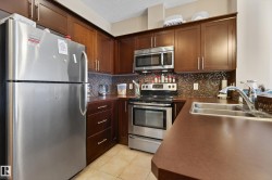 Kitchen featuring wood-finish cabinetry, stainless steel appliances, mosaic tile backsplash, and a double-basin sink - 