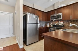 Kitchen featuring dark wood cabinetry, stainless steel appliances, a mosaic tile backsplash, and a double basin sink - 