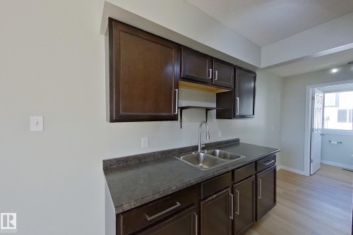 The kitchen features dark wood cabinetry, a double basin stainless steel sink with a gooseneck faucet, and a grey countertop - 184 Cornell Court, Edmonton, AB - Indoor Photo Showing Kitchen With Double Sink