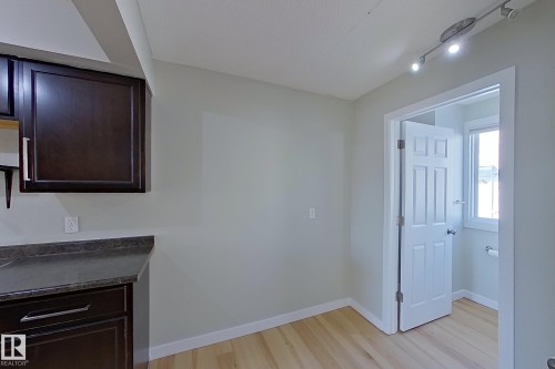 The kitchen area features dark wood cabinetry with chrome hardware, dark countertops, and light wood flooring - 184 Cornell Court, Edmonton, AB - Indoor Photo Showing Other Room