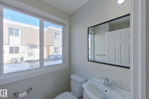 The bathroom features a window providing natural light, a mirror with a black frame, and a white toilet and sink - 184 Cornell Court, Edmonton, AB - Indoor Photo Showing Bathroom