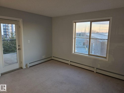 Carpeted room with a large window and a glass-paneled door opening to a private balcony - 310 12045 22 Avenue, Edmonton, AB 