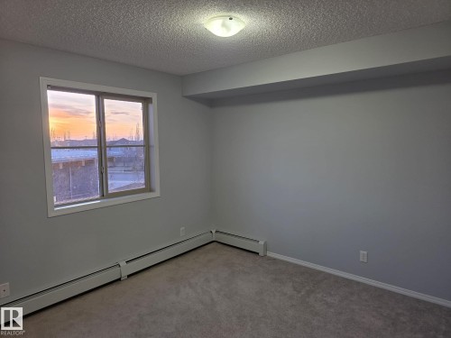Light-filled room featuring a large window, neutral gray walls, and plush carpeting - 310 12045 22 Avenue, Edmonton, AB 