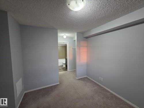 Carpeted room with light gray walls, white trim, and a ceiling-mounted light fixture - 310 12045 22 Avenue, Edmonton, AB 