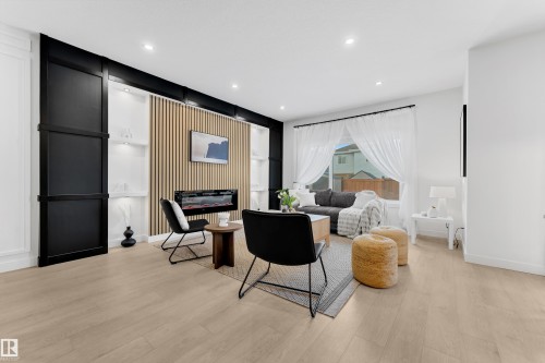 Living room featuring light-colored flooring, a large window with sheer curtains, a built-in entertainment unit with a decorative fireplace, and recessed lighting - 1089 Starling Drive, Edmonton, AB - Indoor