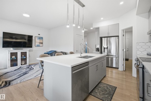 Open-concept kitchen featuring a central island with integrated sink, stainless steel appliances, light wood-finish flooring, recessed lighting, and a geometric tile backsplash - 7782 174A Avenue, Edmonton, AB - Indoor Photo Showing Kitchen With Double Sink With Upgraded Kitchen