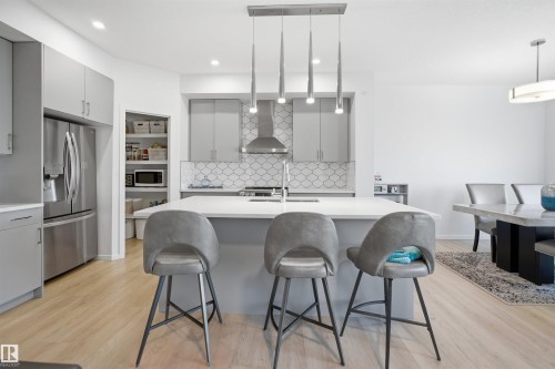 Modern kitchen featuring light gray cabinetry, stainless steel appliances, a center island with seating, a geometric tile backsplash, and light wood-finish flooring - 7782 174A Avenue, Edmonton, AB - Indoor Photo Showing Other Room