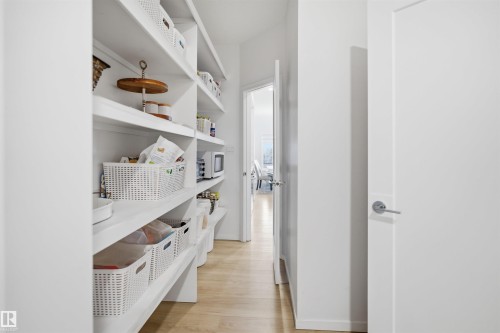Walk-in pantry featuring extensive built-in shelving, light wood-finish flooring, and bright white walls - 7782 174A Avenue, Edmonton, AB - Indoor Photo Showing Other Room