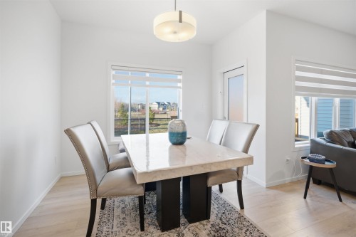 Dining area featuring light wood-finish flooring, a contemporary pendant light fixture, and large windows with horizontal blinds - 7782 174A Avenue, Edmonton, AB - Indoor Photo Showing Dining Room