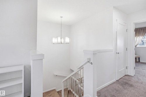 Upper-level landing featuring a chandelier light fixture, neutral carpeting, white interior doors, and a staircase with a metal railing - 7782 174A Avenue, Edmonton, AB - Indoor Photo Showing Other Room