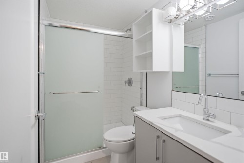 Bathroom featuring a frosted glass shower enclosure, white subway tile surround, contemporary vanity with integrated sink, chrome fixtures, and built-in shelving - 7782 174A Avenue, Edmonton, AB - Indoor Photo Showing Bathroom