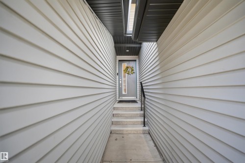 Modern entryway featuring light-colored siding, a dark soffit, and concrete steps with a black metal handrail - 7782 174A Avenue, Edmonton, AB - Outdoor With Exterior