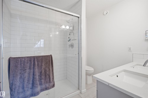 Bathroom featuring a glass-enclosed shower with white subway tile, a dual vanity with undermount sinks and white countertops, and light tile flooring - 7782 174A Avenue, Edmonton, AB - Indoor Photo Showing Bathroom