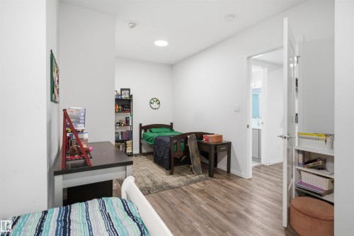 Spacious room featuring wood-finish flooring, white walls, recessed lighting, and a white interior door providing access to a bathroom with a modern vanity - 7782 174A Avenue, Edmonton, AB - Indoor